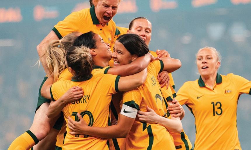 Seven women in the Australian soccer uniform all cheering and hugging one another.