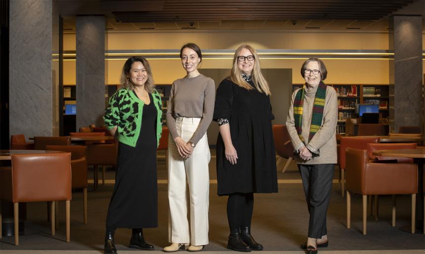 Four people standing in front of chairs and tables.