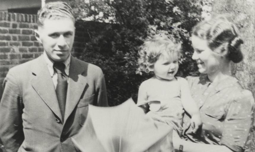A black and white image of a man standing next to a woman holding a child and an umbrella.
