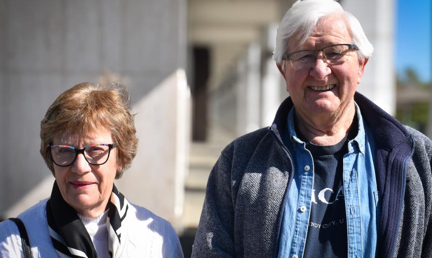A man and woman, both Library volunteers, standing outside the Library on a sunny day smiling