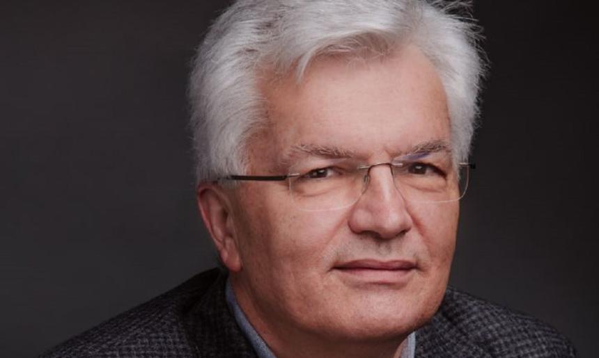 A headshot of a man with white hair and wearing glasses.