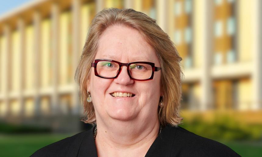 Woman with short blonde hair and dark red square glasses standing in front of the National Library