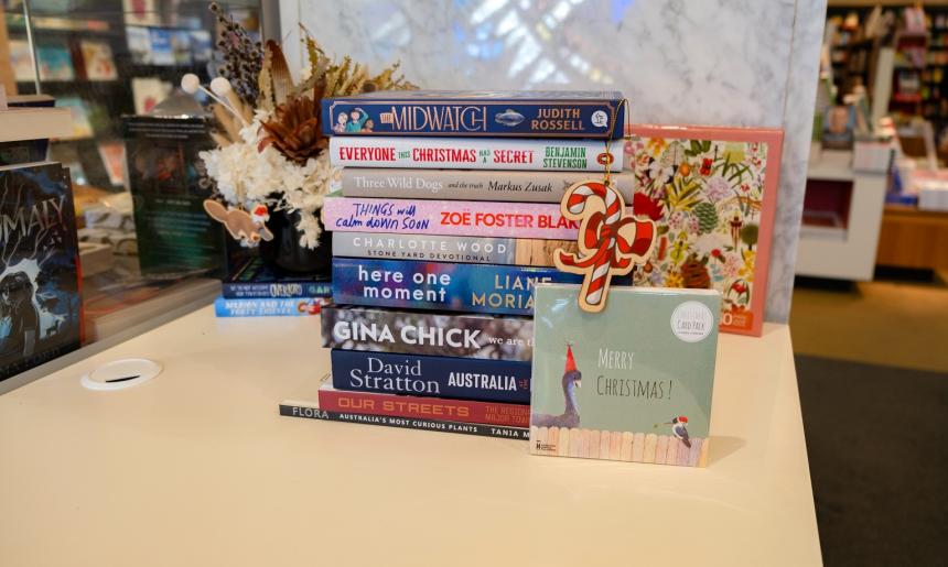 Stack of books, some with Christmas themes, with a greeting card that reads 'Merry Christmas' and a candy cane ornament