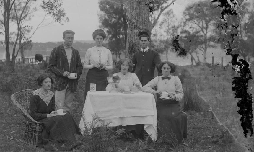 Group of two men and three women sitting around an outdoor table with teacups