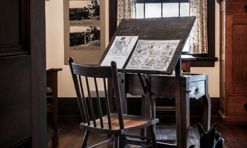 Easel, with two illustrated pages on it, and chair in May Gibbs' studio in Nutcote