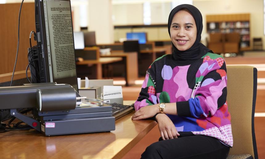 Dr Rafiqa Qurrata A'yun sitting at a computer in the Main Reading Room and smiling