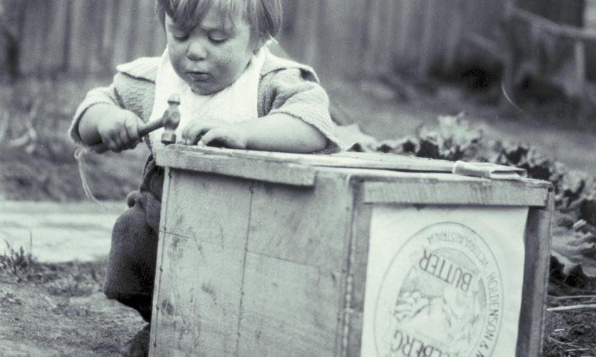 Black and white photo of a small child playing with a wooden box and a hammer