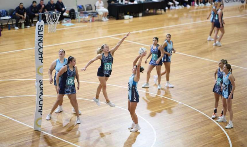 Action shot during a netball game as a women jumps up to prevent another from scoring