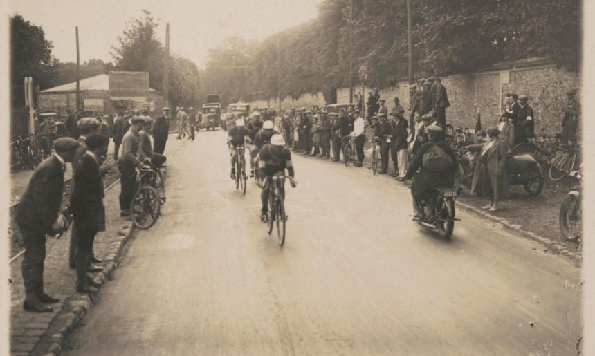 A black and white image of cyclists racing on a street lined by spectators