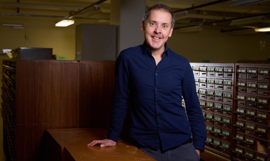 Prof. John Morrissey, 2025 National Library of Australia Stokes Fellow leaning on a table in one of the reading rooms. 