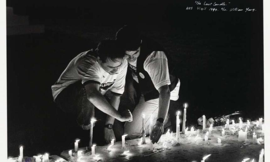 Two men kneel before rows of candles on the ground