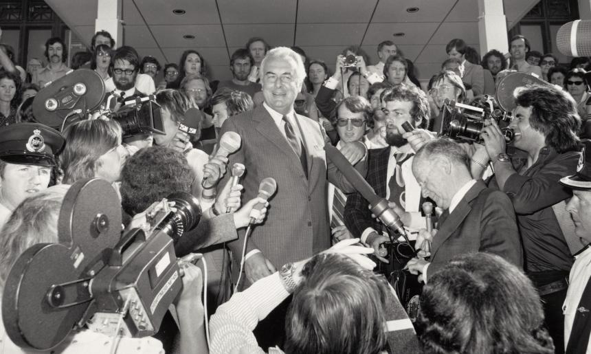 Black and white photo of Gough Whitlam speaking at Parliament House surrounded by reporters