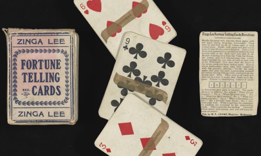 Three objects lie across this image on a black background. A card box, three playing cards with fortunes written on them, and an instruction sheet.