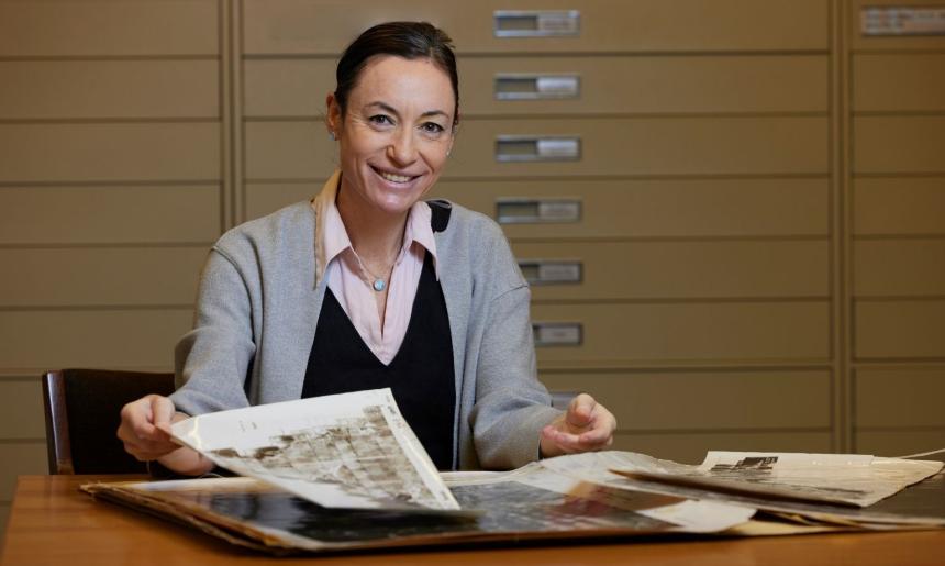 A woman in a grey jacket with a pink and black undershirt holding sepia collection material in the Special Collections Reading Room at the National Library of Australia