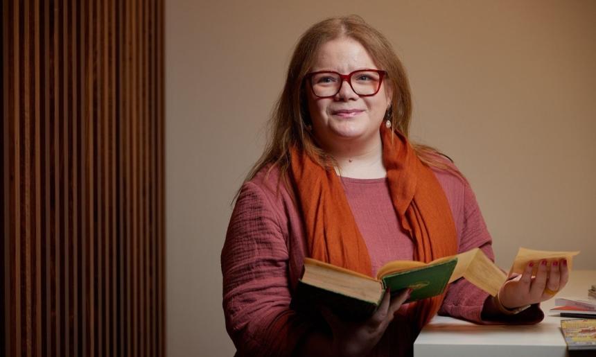 A woman with red hair and glasses holding a book with the fold out pages