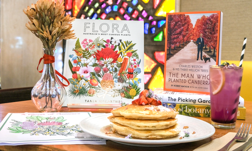 Table at Bookplate cafe with special menu items, kids activity sheets and books for Floriade with colourful stained glass windows in the background