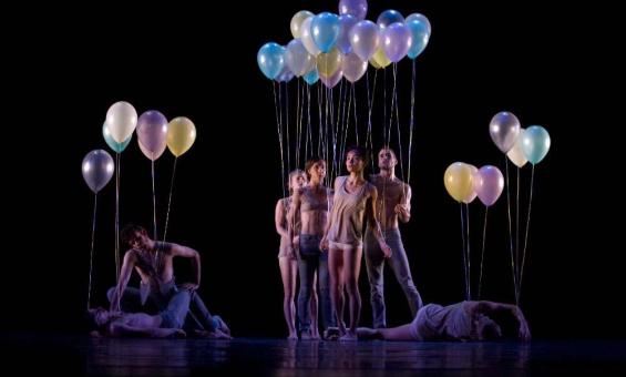 Dancers standing, crouching, and laying down holding balloons