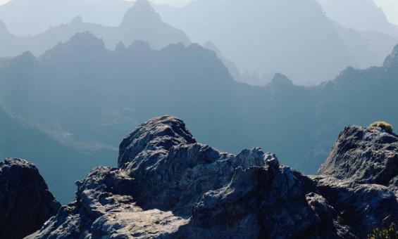 A sweeping landscape of a mountain range. The mountains are craggy and rocky. They are covered in mist.