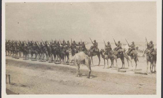 Sepia photograph of World War One soldiers mounted on camels lined up for inspection on the sand
