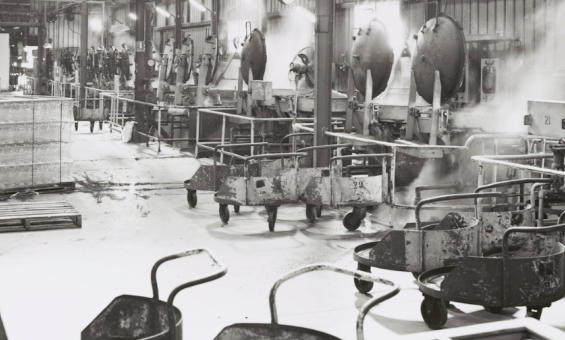 Black and white photo of a factory floor lined with steaming pressure cookers.