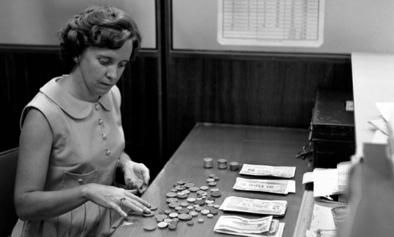Black and white photo of a young woman counting coins and notes at a desk.