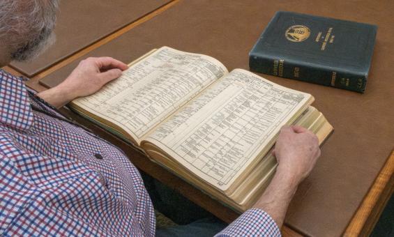 Man reading through a thick, leather-bound book of shipping registers