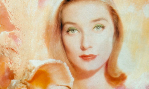 Artistic image of a blonde woman with light eyes smiling slightly in front of a pink and orange background