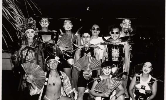 A black-and-white group photo of participants from the Asian Lesbian and Gay Pride Group at the 1994 Mardi Gras. The group wears theatrical costumes with fans and headpieces, posing together with smiling faces, showcasing cultural pride and creative expression.