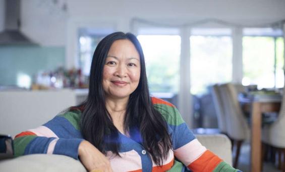 Woman of Chinese heritage sitting on a couch in a nice house, wearing a colourful striped jumper and smiling