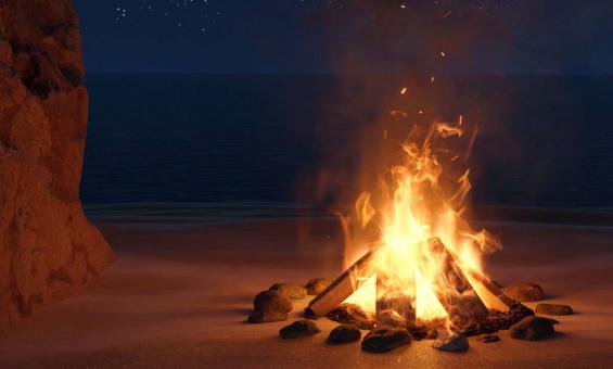 A fire burning on sand with a night sky behind it