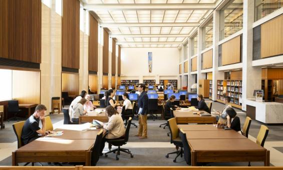 People reading and talking in a large, sunny room at tables, desks and computer stations