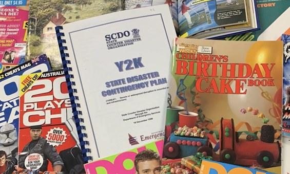 Magazines and books from the 00s and 90s spread out, including the 'Australian Women's Weekly: Children's birthday cake book' and a document titled 'Y2K: State disaster contingency plan'