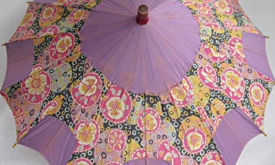 A vintage silk women's umbrella or parasol, which is opened and has alternating panels of mauve and floral design.