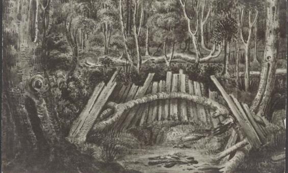 A black-and-white postcard depicting a forest scene with a large wooden structure resembling a natural shelter or barricade. The structure is made from wooden logs and branches, arranged in a semi-circle or arch. The dense forest in the background features tall trees, ferns, and thick underbrush, creating a secluded and mysterious atmosphere. The ground appears rough, with scattered debris and fallen logs. The image is reminiscent of a hidden or protected space within the wilderness.