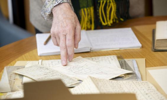 Woman's hand pointing at something on a map on a table with various manuscript material