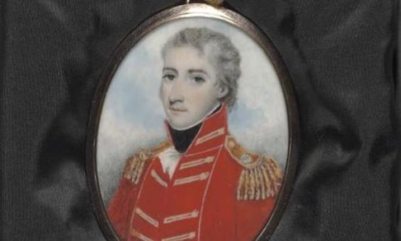 A painted locket portrait of a man in a red military uniform. The locket is resting on some black material.