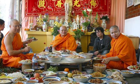 Three Buddhist Monks in orange robes sitting around a large spread of food in a temple