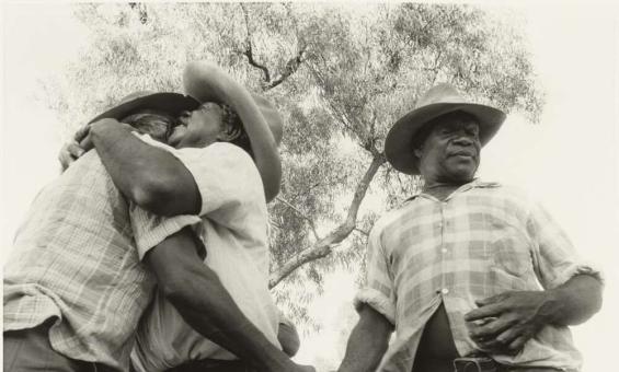 Two men hug and another man shakes one of their hands