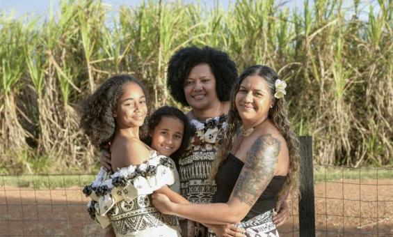 Four Fijian women of various ages wearing dresses smiling and embracing