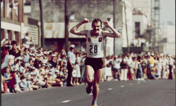 A marathon runner smiles and holds his fists up as he runs