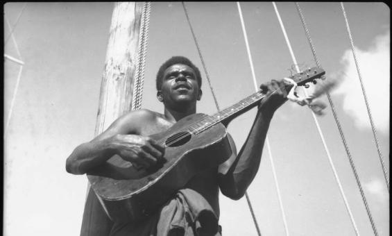 A black and white photo of a man playing a guitar on a boat