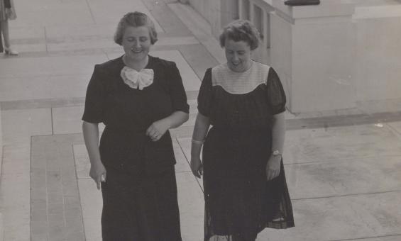 Black and white photo of two women, Dorothy Tangney and Enid Lyons, walking together towards the entrance of Old Parliament House 