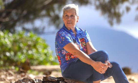 Fijian Australian woman with short grey hair sitting on a rock on a beach