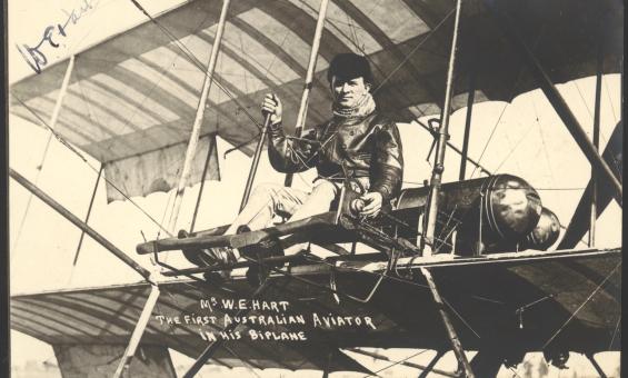 Man in a leather jacket and cap seated in an old biplane