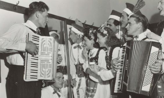 Group of men and women wearing traditional Polish clothing playing various instruments and smiling