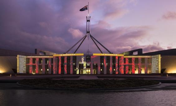 Parliament House at sunset, lit up with an image of Queen Elizabeth II and the words 'In memoriam'.