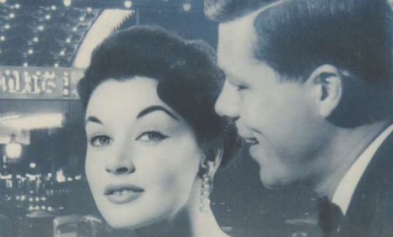 Man and woman in fancy dress in front of a train station at night, with text reading 'in town tonight ... by train'