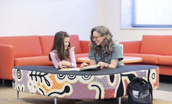 Woman and child smiling as they read a book in the kid's corner of the main reading room