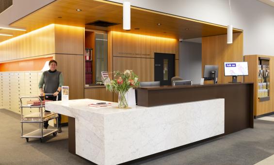 Librarian wheeling a trolley with collection material around the Newspapers & Family History Zone desk