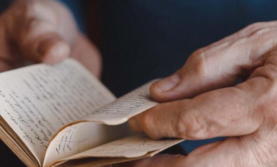 Close-up of a person's hands carefully turning the pages of an old, handwritten journal.